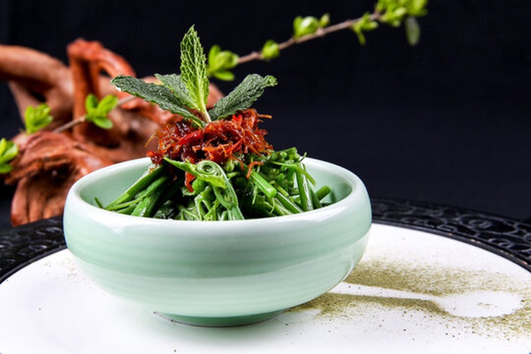 一碗色彩鲜明的凉拌菜,包含切段的翠绿十香菜与亮绿色薄荷叶,混合红椒丝与白芝麻,置于陶瓷碗中,体现两种香草在实际烹饪中的协同应用 十香菜与薄荷混合凉拌菜