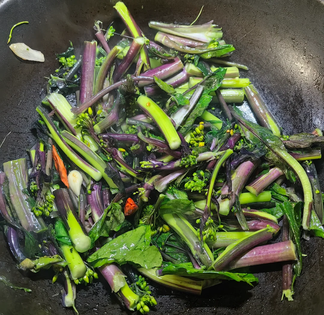 一盘刚出锅的蒜蓉炒紫菜苔,紫红色茎条整齐排列,泛着油光,蒜末均匀点缀其间,背景为白色瓷盘与木制餐桌,体现家庭厨房温馨氛围 紫菜苔家常菜肴成品图