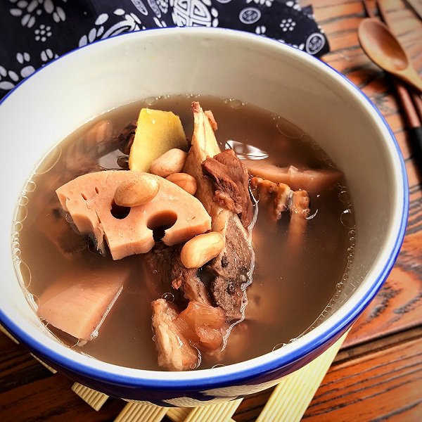 一个陶瓷砂锅正放在炉灶上慢火炖煮,锅内翻滚着乳白色的莲藕排骨汤,几块淡黄色的莲藕清晰可见,筷子轻压即碎,呈现出典型的粉糯状态;旁边摆放着原料盘,含藕片、排骨和姜片 家庭厨房中正在炖煮莲藕排骨汤的砂锅特写