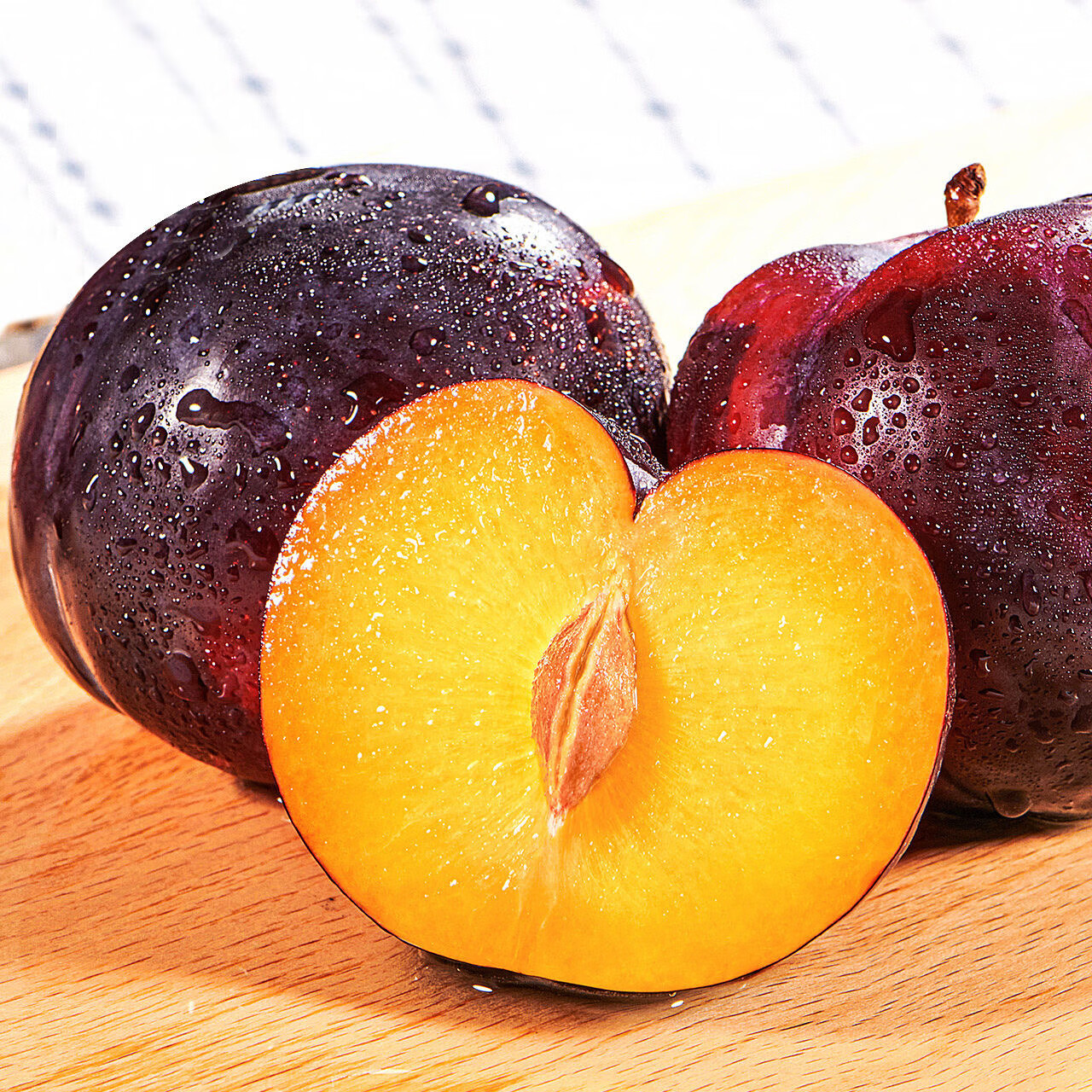 一颗切开的黑霸王李子,果皮呈深紫黑色,果肉为淡黄色至琥珀色,质地紧实多汁,剖面可见清晰的维管束结构,果汁微微渗出,旁边摆放一把不锈钢水果刀和白色瓷盘 黑霸王李子切开特写