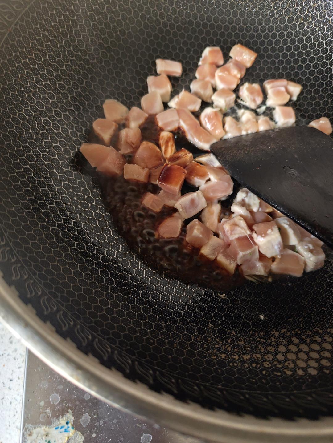 一位家庭主妇正在灶台前翻炒锅中的鸡腿块,锅中已有明显焦糖化反应的大葱段与鸡腿一起炖煮,汤汁浓郁呈红褐色;旁边放有切好的葱段、姜片和调料瓶;背景为整洁的现代厨房环境,窗户透进自然光 家庭厨房中正在烹饪鸡腿大葱菜肴的场景