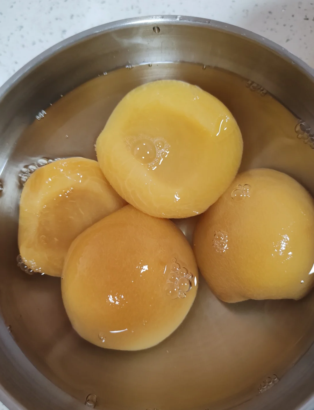 黄桃块正在糖水中炖煮,锅中冒出微微气泡,糖水颜色金黄 正在炖煮的黄桃罐头