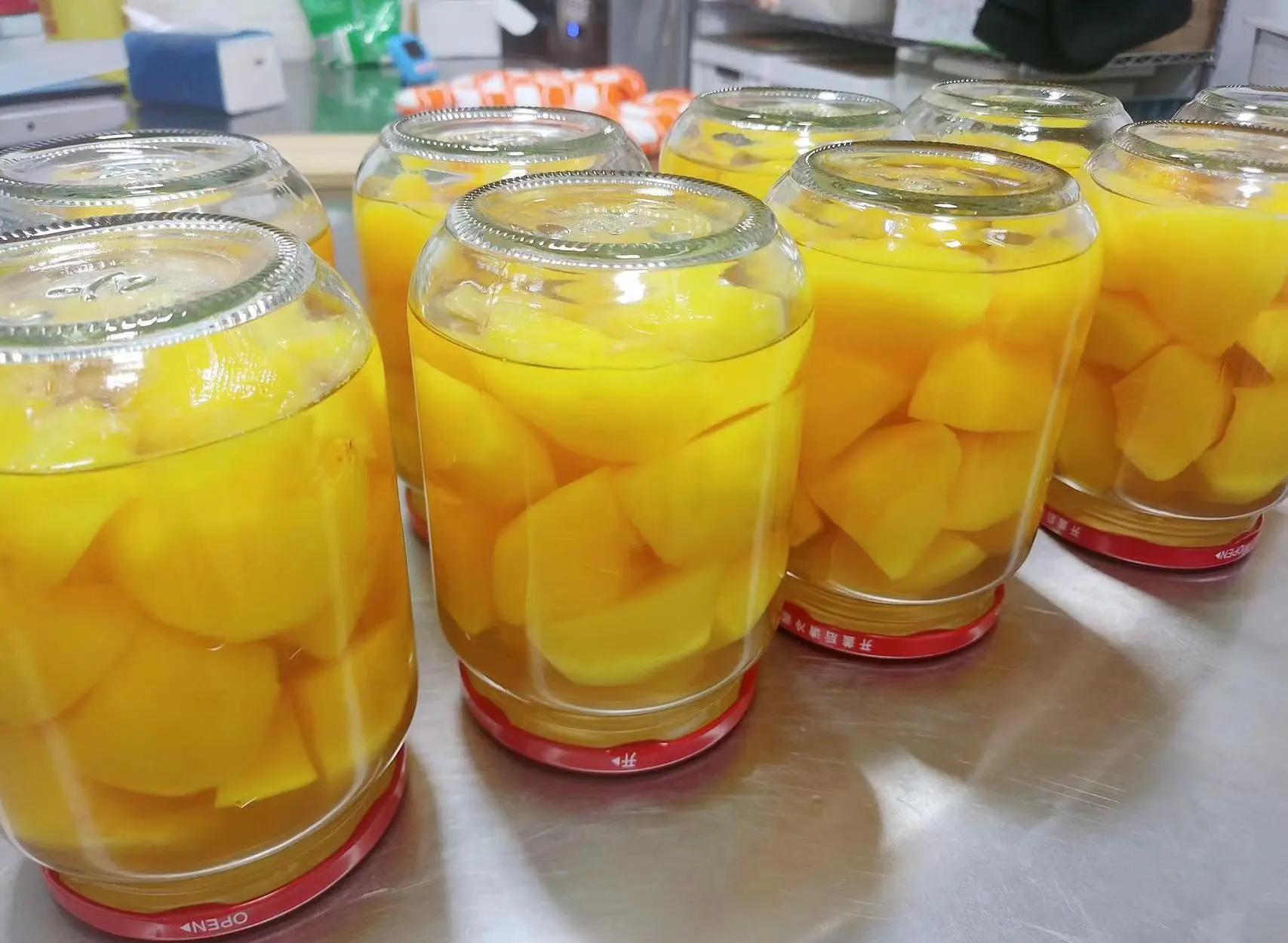 一排透明玻璃罐整齐排列在木架上,罐内盛放着金黄色的黄桃块和清澈糖水,标签注明‘自制黄桃罐头’和制作日期,背景为阳光洒入的厨房窗台 黄桃罐头成品展示