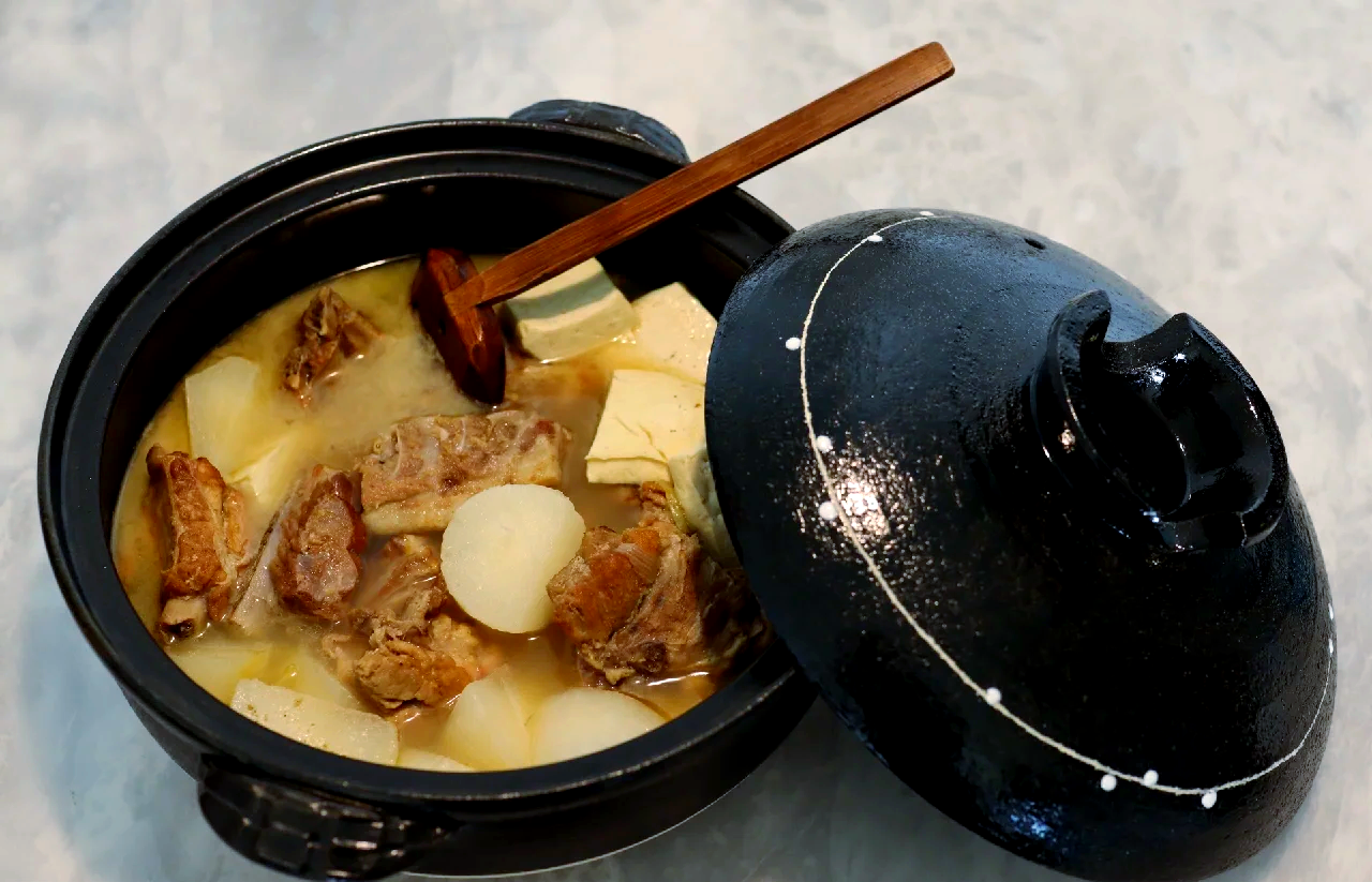 厨师正在厨房用砂锅慢炖牛肉与切块萝卜