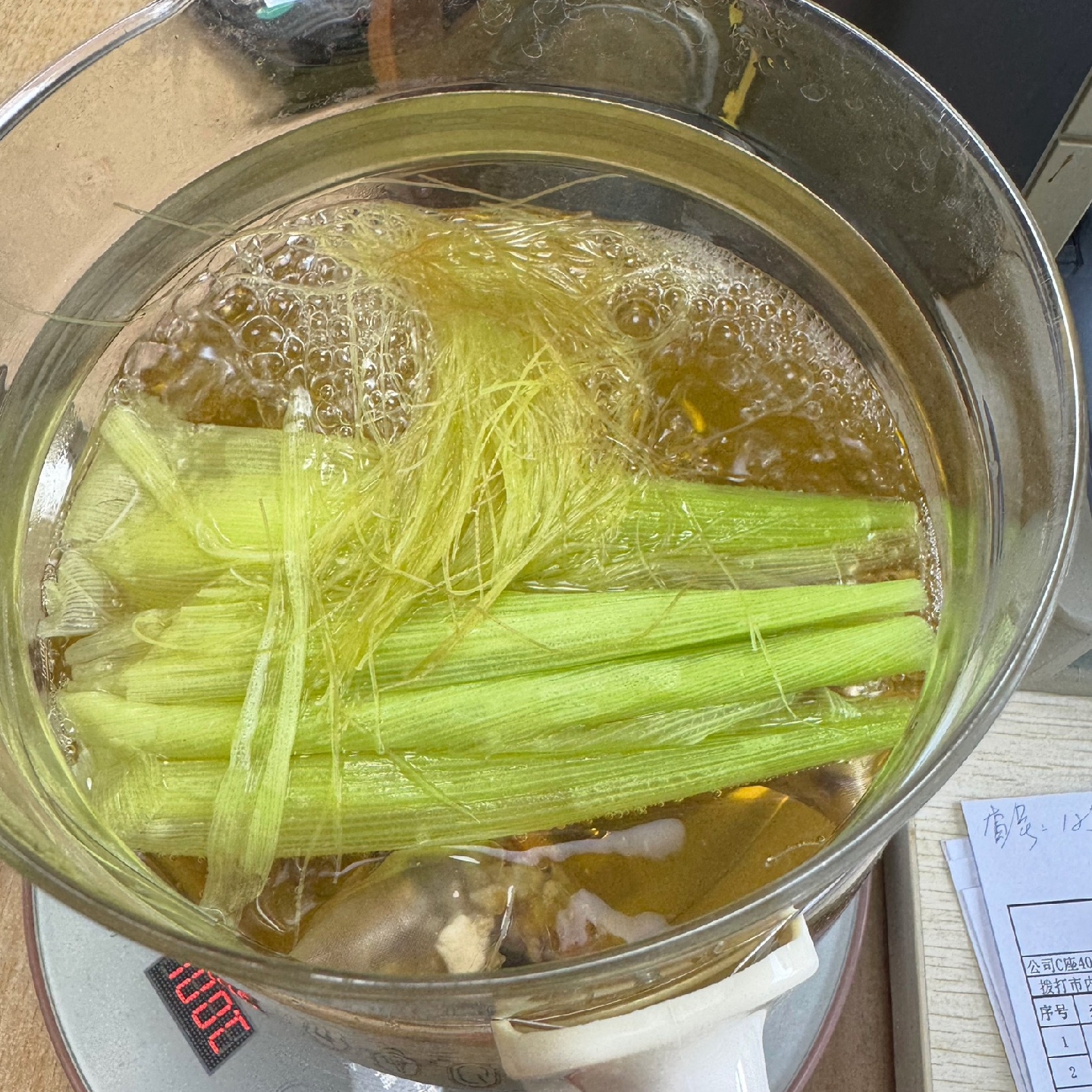 煮玉米的汤水倒入玻璃杯中，呈淡黄色，旁边放着玉米棒和几根玉米须