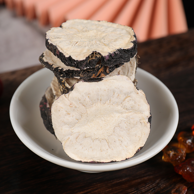 一个白色瓷碗中盛放黑色细腻的黑玛卡粉末,旁边放置一勺量具,一杯冲泡好的浅褐色玛卡牛奶饮品置于木桌上,周围点缀枸杞、莲子和银耳,整体呈现自然健康的饮食场景 黑玛卡粉末与饮品搭配示意图