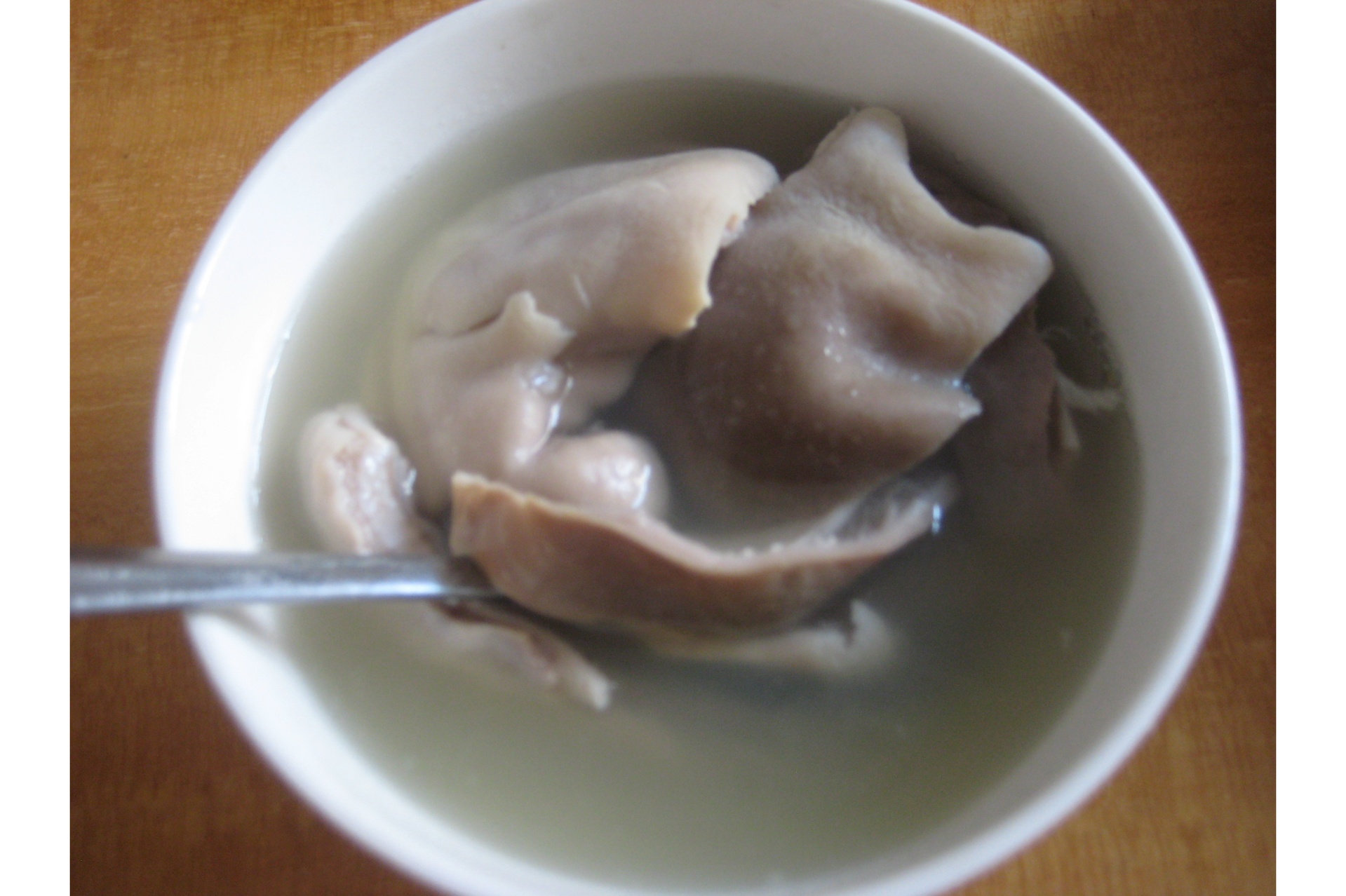 一碗热气腾腾的乳白色猪肚汤,碗中可见清晰的猪肚条、胡萝卜块和玉米段,表面漂浮着细小油珠和葱花,背景为木质餐桌,氛围温馨 白胡椒猪肚汤成品盛碗特写