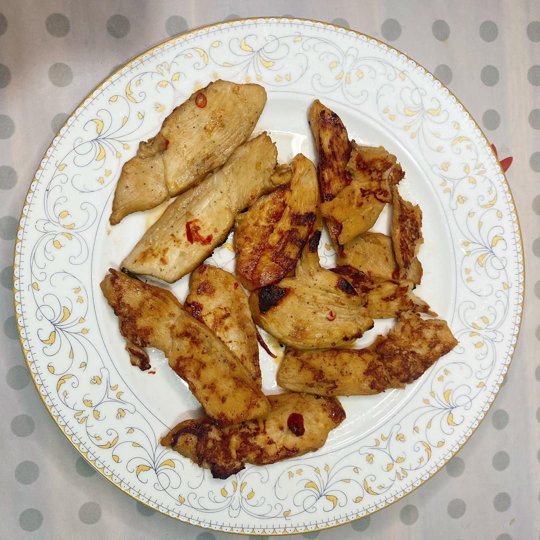 白色陶瓷盘中摆放着斜切的黑胡椒香煎鸡胸肉,肉质洁白带金黄焦边,周围点缀翠绿西兰花与橙黄胡萝卜片,顶部撒有现磨黑胡椒粒,旁边配有半个柠檬和木制餐刀,整体风格清新健康 成品摆盘展示