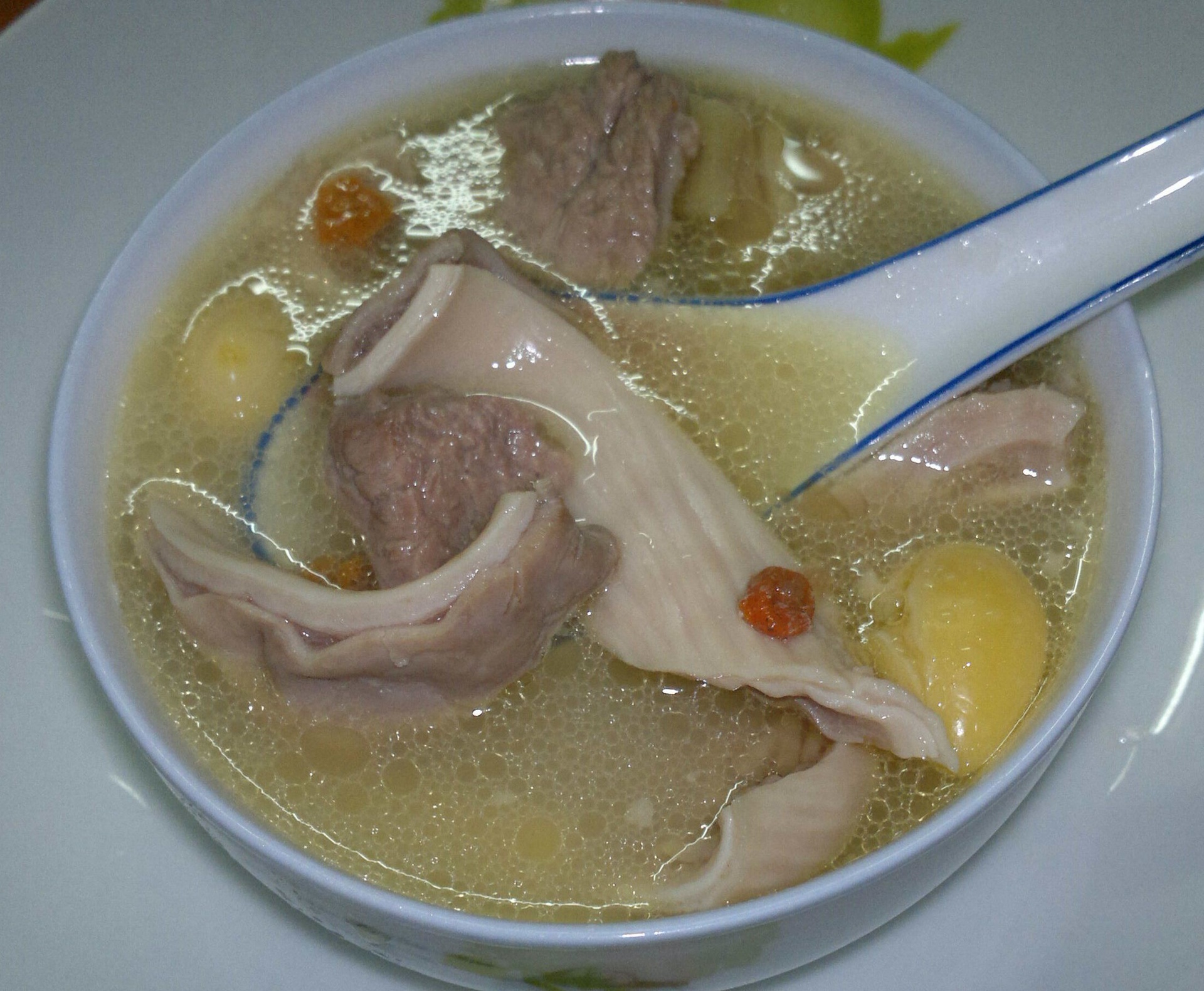 一碗热气腾腾的传统白胡椒猪肚汤,汤色乳白,可见猪肚块和浮游的胡椒颗粒,旁边摆放瓷勺和青花碗,体现中式养生饮食文化氛围 白胡椒猪肚汤成品图