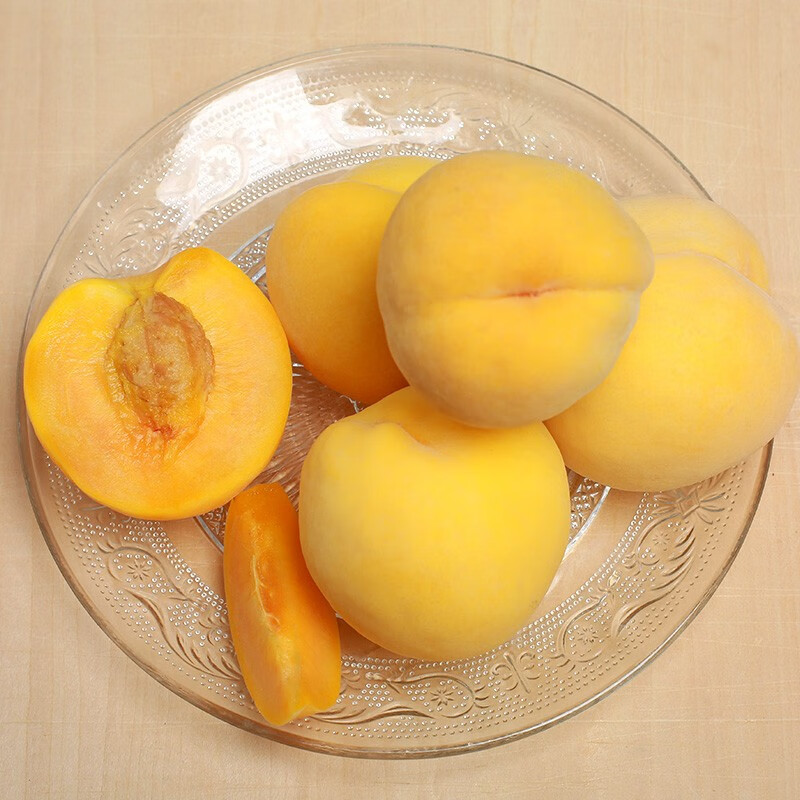 一个被横向切开的新鲜黄桃,露出金黄色的果肉和较小的果核,果肉纹理细腻,汁水欲滴,周围散落着几片桃瓣和一片绿叶,背景为木质餐桌,突出自然新鲜感 黄桃切开特写