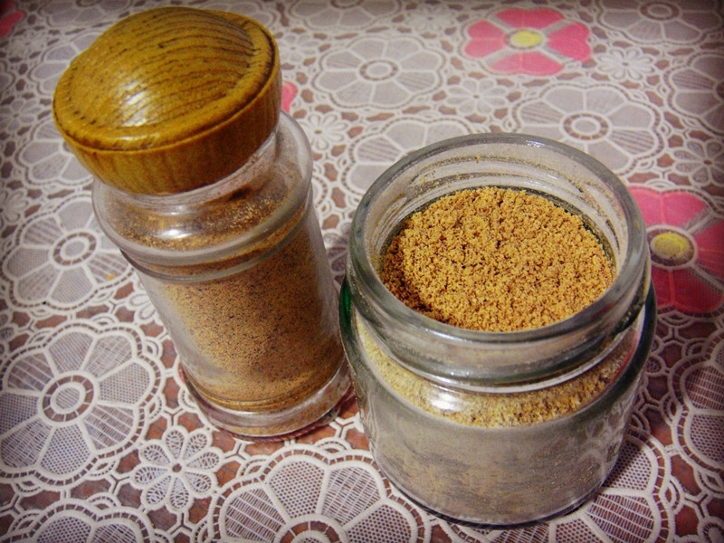 侧柏籽香料粉装在玻璃罐中,背景为木质桌面,旁边摆放香料包和调味勺 侧柏籽香料成品展示