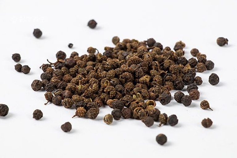 一位身穿白大褂的中医师正在中药柜前手持一小袋干花椒,向患者讲解其性味归经,背景可见‘花椒’‘温中止痛’等标签,体现专业科普场景 中医师在药房讲解花椒药性
