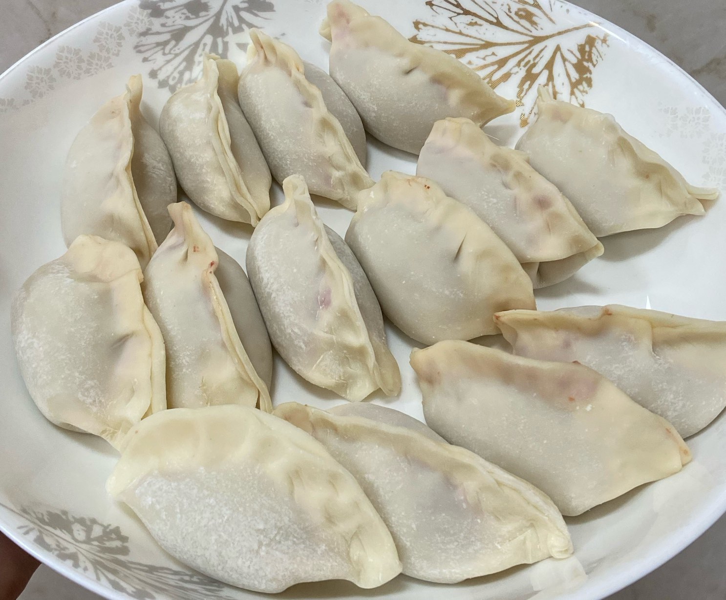 一盘刚出锅的白色水饺,整齐排列在瓷盘中,部分饺子已剖开展示内馅,可见翠绿色的松花菜与金黄色鸡蛋混合的馅心,表面略带油光,旁边配有醋碟与小葱段,整体呈现家庭厨房温馨氛围 松花菜饺子成品图