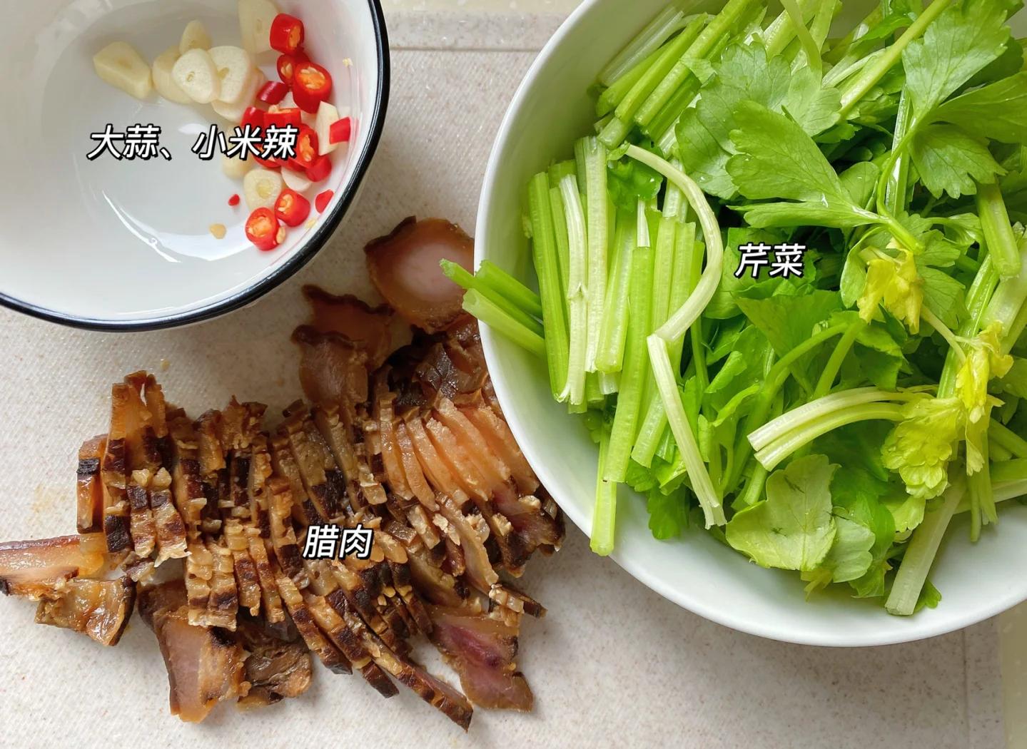 一名厨师正在案板上处理西芹和腊肉:左侧是去皮后的翠绿西芹被切成斜段,右侧是刚蒸好的腊肉正在被切成均匀的薄片,旁边摆放着小碗盛放的姜蒜末 西芹与腊肉的预处理过程
