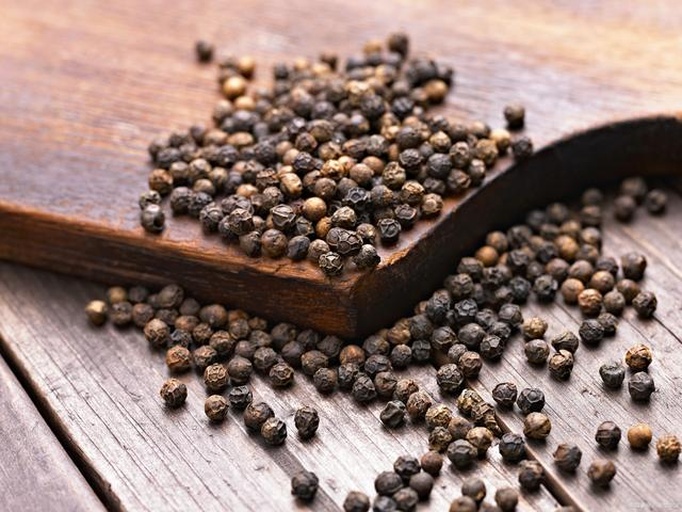 一盘深褐色的整粒黑胡椒散放在木质砧板上,旁边是一个不锈钢手动研磨器,背景为厨房操作台,光线柔和自然,突出香料的新鲜质感 黑胡椒粒与研磨器特写