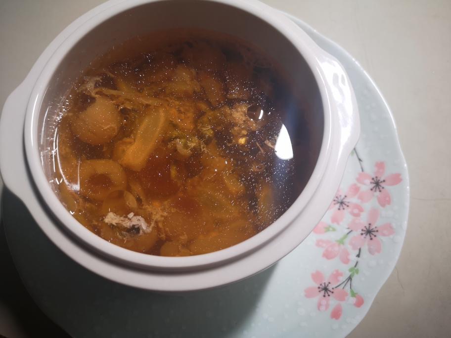 暖色调俯拍:白色汤碗中盛满清亮琥珀色高汤,浮着柔嫩蛋花、墨绿紫菜丝与洁白花蛤肉,表面淋有金黄香油光泽,撒翠绿葱花,背景为木质餐桌与竹制汤勺 家常紫菜花蛤汤成品特写