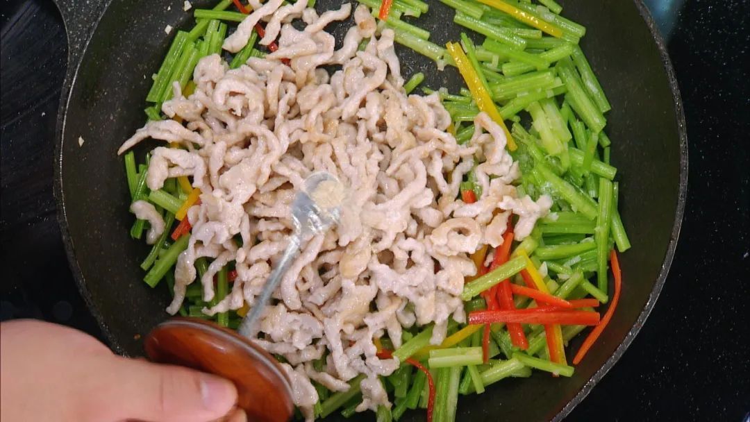 一位家庭主妇在现代化厨房中使用铁锅翻炒芹菜与羊肉,锅中食材翻腾,伴有轻微油烟,左手持锅柄,右手用铲子翻拌,背景可见调料瓶与计时器,展现真实烹饪过程 家庭厨房中正在翻炒芹菜羊肉的场景