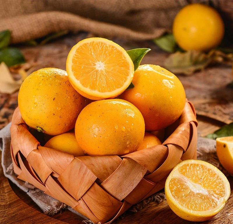 多个新鲜橙子整齐地摆放在一个原色竹编篮子中,背景为厨房的木质台面和灰白色墙壁,光线柔和自然,营造出温馨居家氛围 橙子在竹篮中整齐摆放在阴凉角落