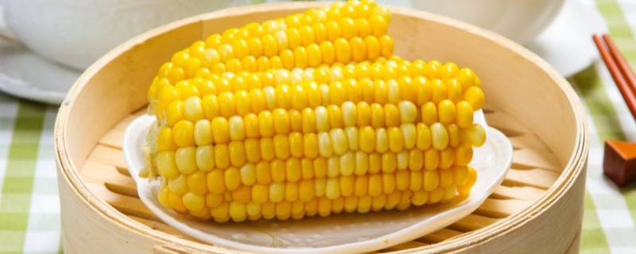 一盘刚出锅的蒸糯玉米,金黄色泽,表面略带水汽,玉米粒饱满紧实,散发热气,旁边配有小碟酱油和葱花,展示家庭健康早餐搭配 蒸熟的糯玉米摆盘特写