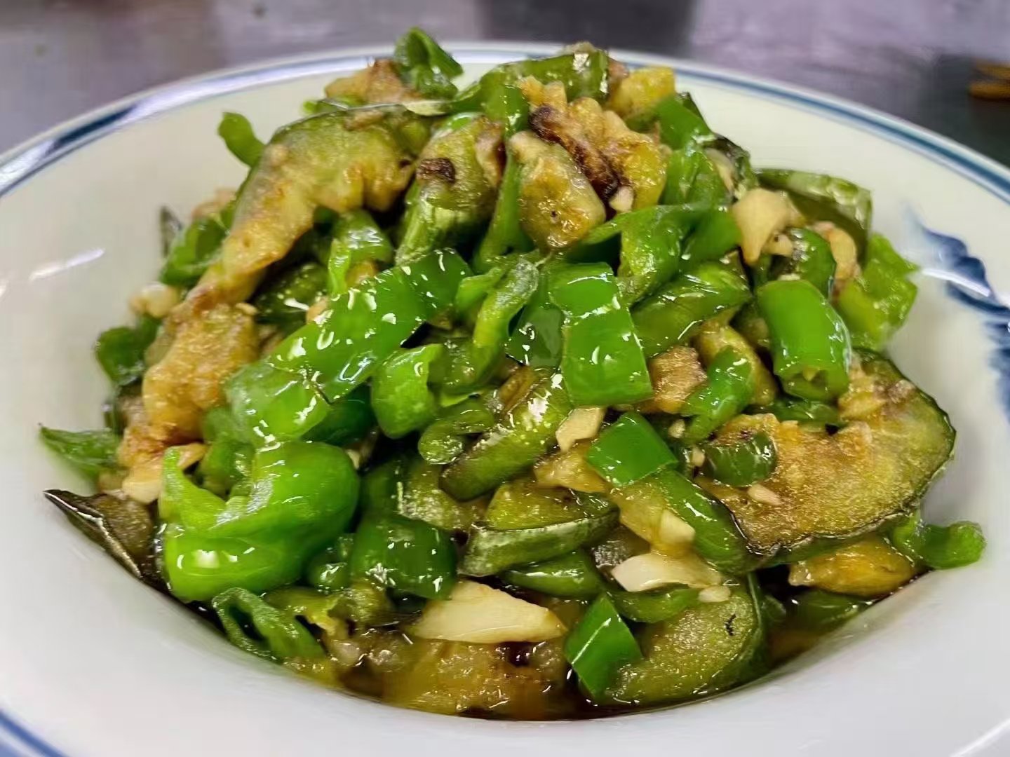 成品小米椒炒茄子盛放在白色瓷盘中，色泽鲜亮，香气扑鼻