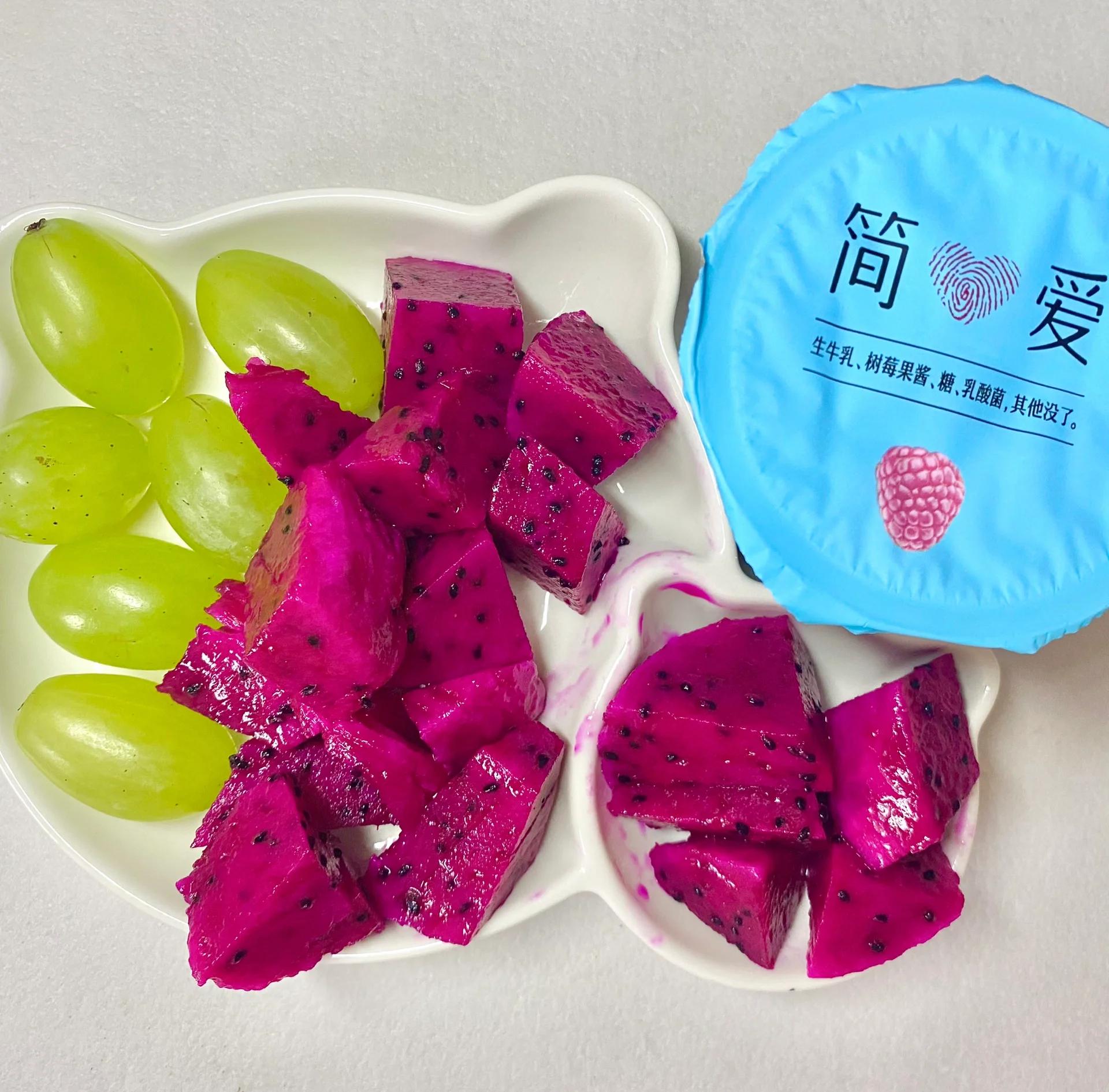 一张餐桌上的早餐拼盘,包含半颗挖出果肉的红心火龙果、酸奶杯、燕麦片、坚果和蓝莓,旁边放着一把木勺,阳光透过窗户洒在食物上,营造健康生活方式的温馨氛围 红心火龙果日常食用场景