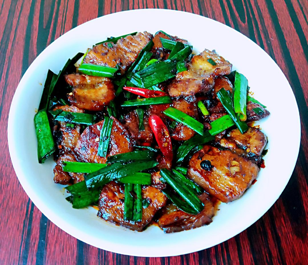 厨房场景：中式铁锅内蒜苗与薄羊肉片同炒，油光润泽，蒜苗翠绿不萎，羊肉呈浅褐色，锅边有少量姜丝与干辣椒段，展现经典温补搭配方式