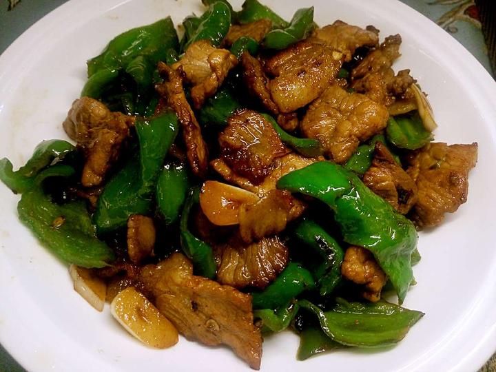 中式厨房实拍:案板上摆放三组食材——左侧为洗净切段的青美人椒(段长约3cm,断面翠绿饱满,汁水丰盈);中间为蒜末与姜丝;右侧为清炒后的成菜(色泽鲜亮,椒段挺括不软烂,佐证其果肉厚度与耐热性);背景可见厨师正在翻炒,体现其在鲜食烹饪中的主流应用 青美人椒在厨房应用场景图