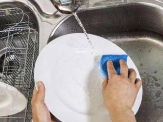 一位家庭主妇正在厨房水槽中用流动清水冲洗泡发后的海带,双手轻柔搓洗表面,背景有剪刀、砧板和碗具 厨房中清洗海带的过程