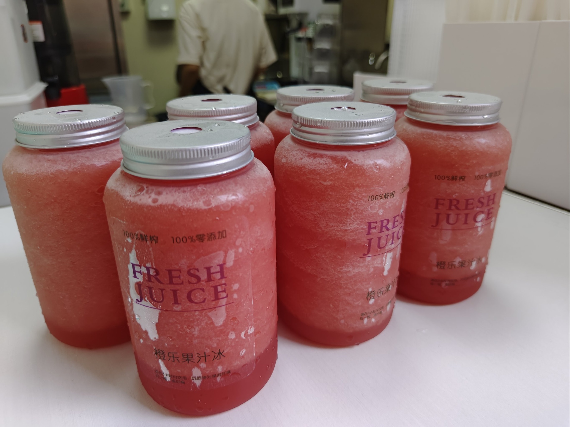 现代超市冷柜中陈列着多个品牌的瓶装苹果汁,标签标注‘100%纯果汁’,旁边篮子里放着新鲜红富士苹果,两者形成鲜明对比,象征加工与天然的区别 超市货架上摆放着多种包装苹果汁产品与旁边的新鲜苹果对比场景