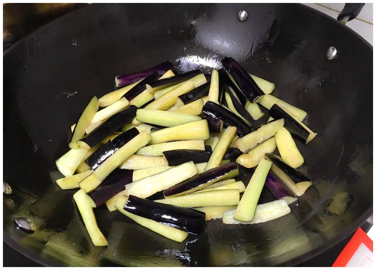 中式炒锅内正在翻炒茄子，锅气升腾，茄子呈微金黄色，蒜末清晰可见，灶台为家用燃气炉，体现真实家庭烹饪场景