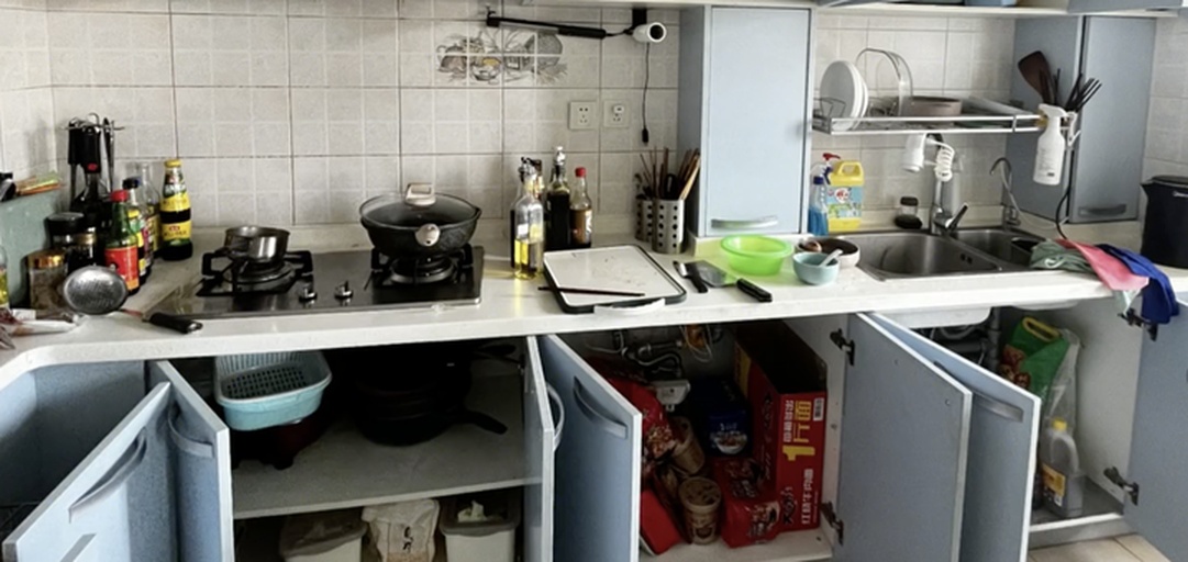 左半部分为现代厨房操作台,摆放着装有翠绿蒜苗的竹篮、砧板和刀具;右半部分为阳台一角,摆放着盛开花朵的水仙盆栽,花盆旁立有‘观赏植物 请勿食用’的小牌子 家庭厨房与阳台场景对比图