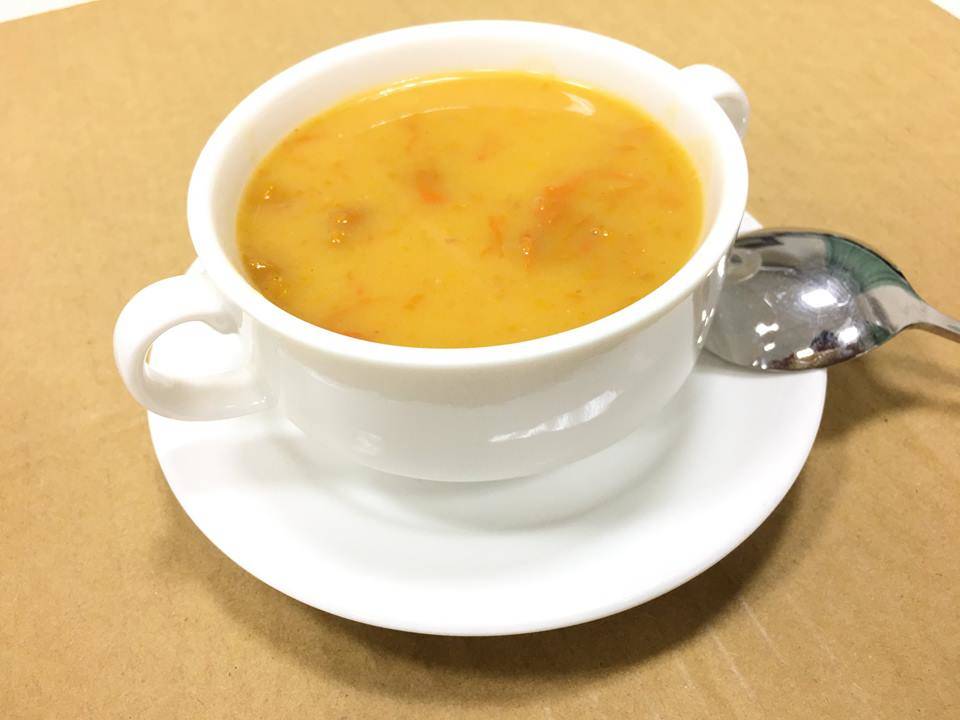 一碗热气腾腾的奶油南瓜汤摆放在木桌上，旁边配有面包片和绿叶装饰