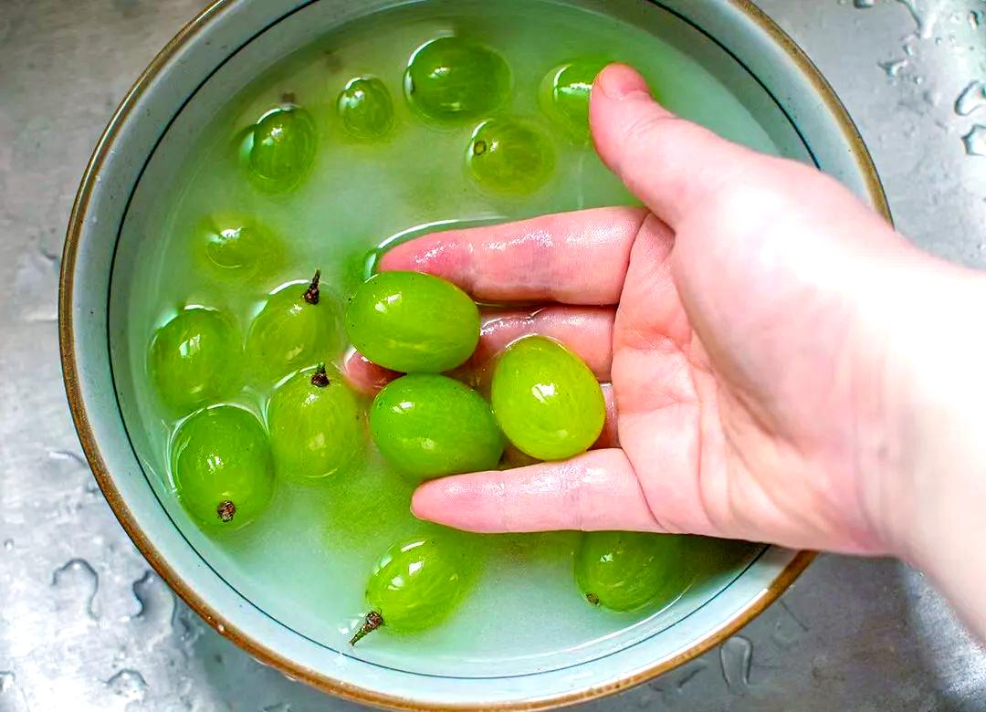 一名家庭主妇正在厨房用盆浸泡黄金梨,旁边摆放着果蔬清洗剂瓶、刷子和去皮刀,强调安全清洗的重要性 图片描述