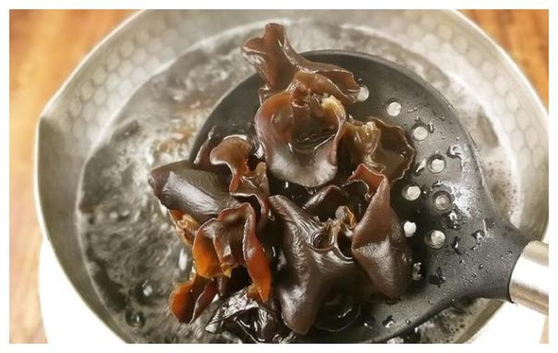 一口不锈钢锅中沸腾的水中正在焯煮黑木耳，木耳呈半透明状漂浮，蒸汽升腾，旁边放着漏勺和冰水碗