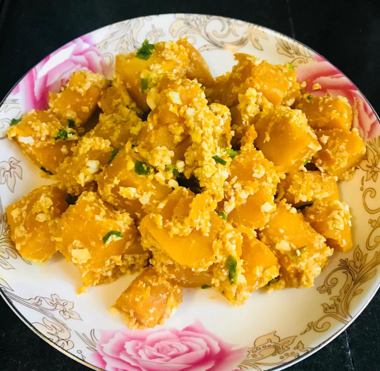 一盘色泽金黄诱人的咸蛋黄炒南瓜,南瓜片裹满细腻泡沫状的咸蛋黄酱,边缘微焦,盛放在白色瓷盘中,背景为中式厨房灶台 咸蛋黄炒南瓜成品图