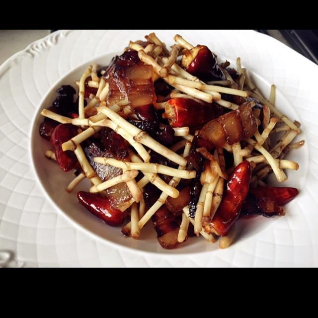 一盘热气腾腾的家常炒苦竹笋,主料为淡黄色的笋片与棕色腊肉片混合翻炒,配以青红椒丝点缀,盛放在白色瓷盘中,背景为木质餐桌与竹制餐具,展现传统中式饮食文化氛围 传统菜肴中的苦竹笋料理