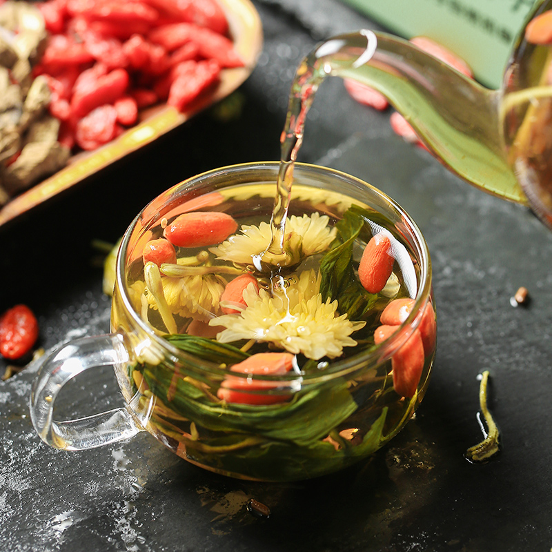 一杯透明玻璃杯中正冲泡着几朵金黄色的野菊花,花瓣舒展,水中泛起淡淡的琥珀色光泽,杯口冒着袅袅热气,旁边摆放一小碟干燥的野菊花,整体画面温馨自然,体现健康养生的生活方式 野菊花茶冲泡效果展示