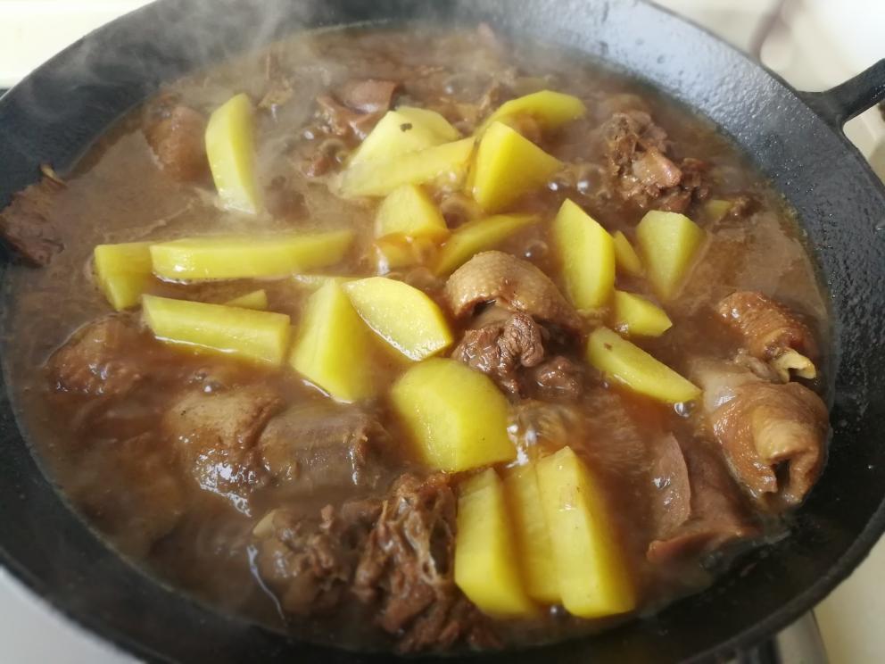 一锅刚出锅的大盘鸡正在被盛入深盘中,鸡肉色泽红亮,土豆块完整饱满,表面裹满浓稠酱汁,周围点缀着青红椒和洋葱,热气腾腾 图片描述