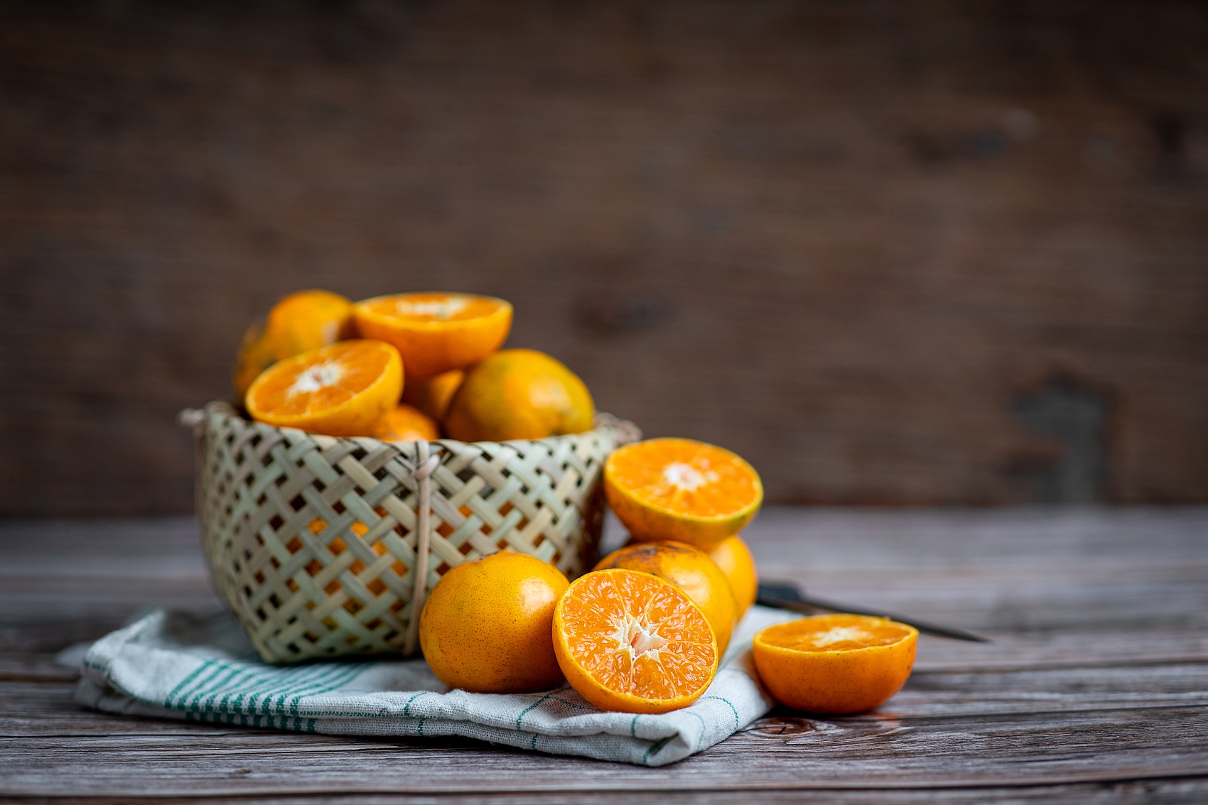 一堆新鲜橙子摆放在木桌上,部分被切开露出多汁的果肉,展示橙子的真实大小与质感 橙子堆放在木质桌面上,背景为自然光线下的厨房环境,橙子表皮光滑有光泽,部分切开展示果肉