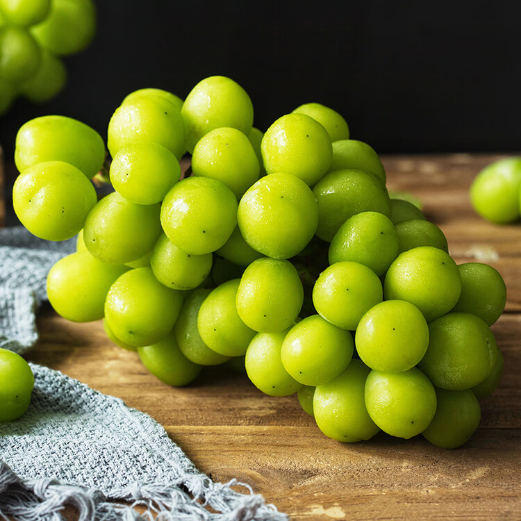 一颗被横向切开的阳光玫瑰葡萄,清晰展示其透明多汁的果肉和几乎无籽的内部结构,果粒晶莹剔透,切口处有汁液微微渗出,背景为浅色木纹桌面,突出水果的新鲜质感与高品质 阳光玫瑰切面细节图