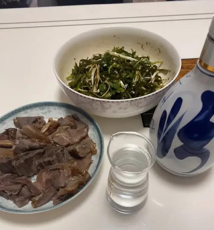 一张乡村风格餐桌上的美食组合:中间是一碗冒着热气的水煮花生,左侧摆放一瓶冰镇啤酒,右侧有凉拌黄瓜和卤蛋,整体氛围温馨惬意,适合家庭聚餐或朋友小酌 水煮花生搭配啤酒与小菜的餐桌全景