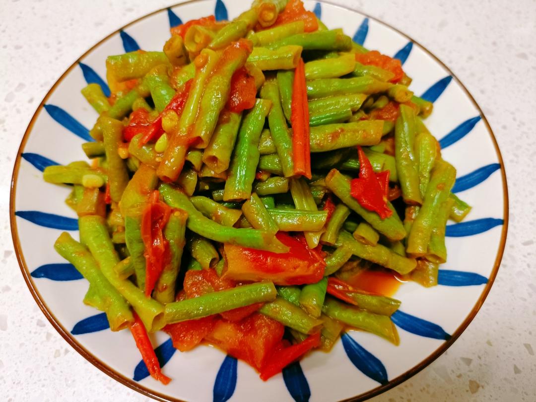 一盘刚出锅的白不老豆角炒西红柿盛放在白色瓷盘中,豆角呈淡绿色,西红柿红润多汁,整体色泽明亮,表面泛着油光,旁边配有木筷和一小碗米饭 成品菜肴特写