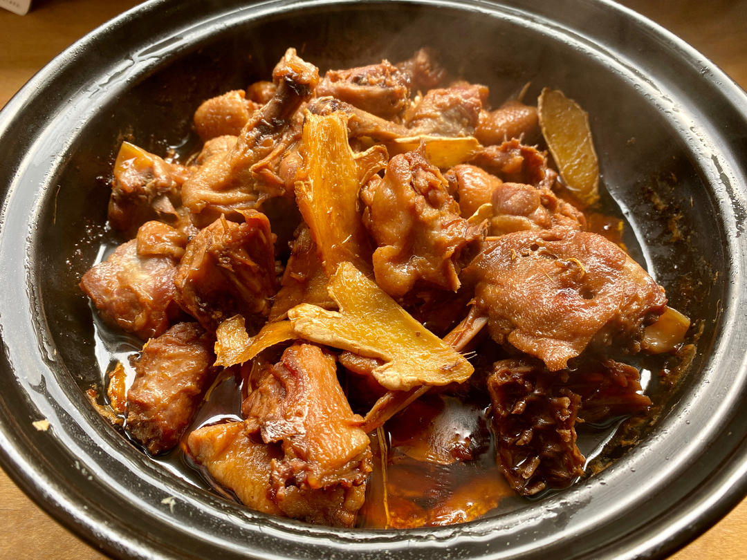 姜酒煮鸡成品特写：琥珀色浓稠汤汁包裹棕红油亮鸡块，可见金黄子姜片与深红红枣嵌于其间，表面浮着细密姜油星点，热气氤氲