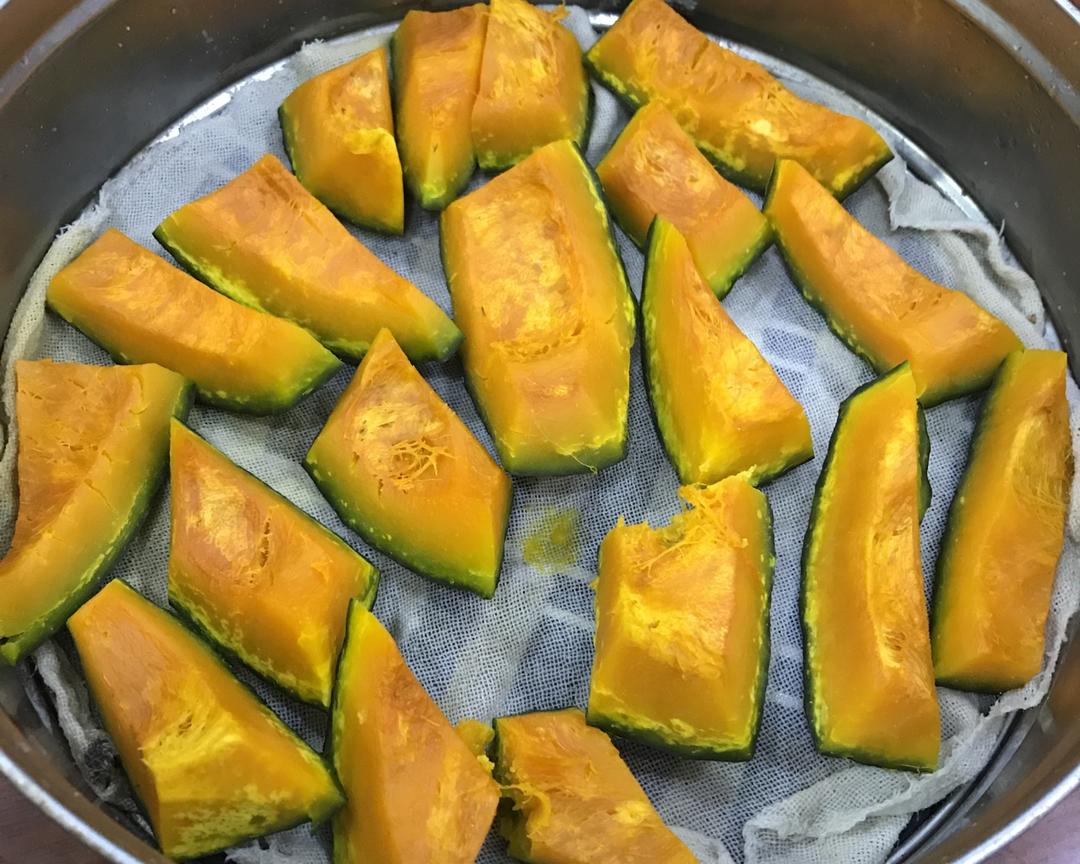 案板上摆放着已去皮的橙黄色南瓜块,大小均匀,整齐排列在竹制蒸屉中,旁边有一把不锈钢勺正在调整位置,展示准备入锅前的状态 南瓜切块摆放过程