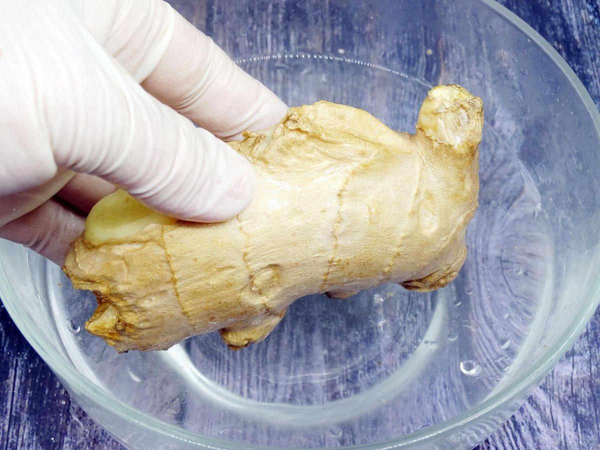 一位手部特写正在用透明玻璃搅拌棒在白色瓷杯中搅动一杯棕黄色液体,杯中有未完全溶解的三七粉末和细小姜粒,蒸汽微微升起,背景为厨房操作台,光线柔和温暖 正在用玻璃杯搅拌三七生姜饮品的过程