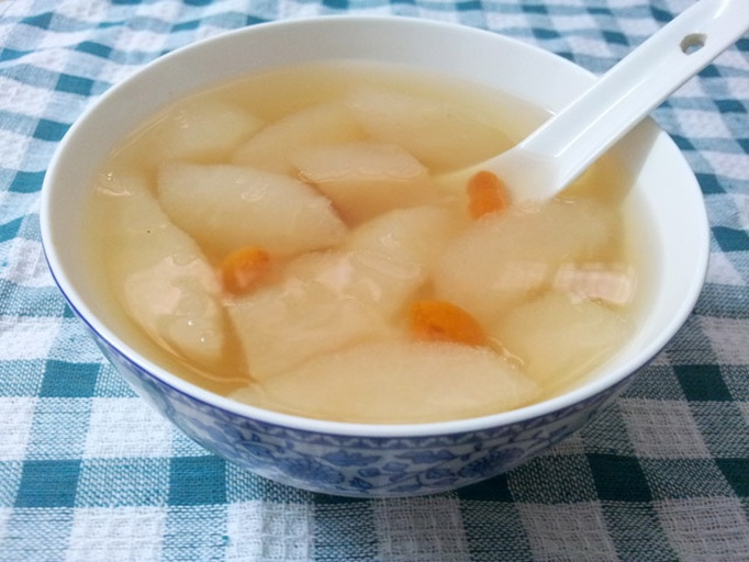 一碗热气腾腾的金桔煮雪梨汤盛在白色瓷碗中，汤色清澈微黄，可见完整的金桔和梨块，表面漂浮少量枸杞