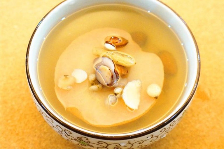 一碗浅色陶瓷碗中盛放两块去核蒸熟的水晶梨,果肉颜色略显透明,表面淋有天然蜂蜜,周围点缀几片薄荷叶,背景为木质餐桌,营造出健康养生氛围 蒸熟水晶梨与蜂蜜搭配图示