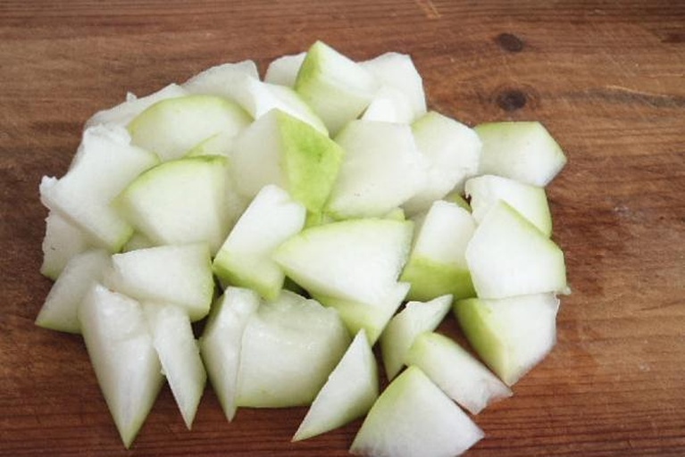 新鲜绿色外皮的冬瓜被横向切成约1厘米厚的圆片,露出洁白多汁的果肉,刀工整齐,背景为木质砧板,光线柔和自然 冬瓜切块特写