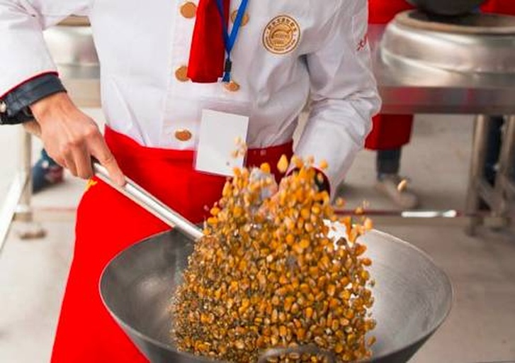 一位厨师正在炉灶前手持锅柄晃动爆裂中的甜玉米花,锅中白色爆米花不断弹跳,蒸汽从锅盖缝隙逸出,厨房环境整洁明亮 爆玉米花过程中动态场景