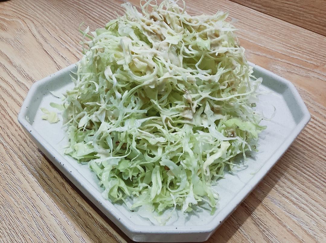 一份精致摆盘的木瓜生菜沙拉，盛放在白色陶瓷盘中，顶部撒有白芝麻和杏仁片，背景虚化，突出食物色彩对比